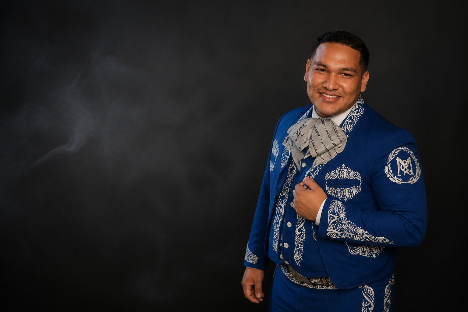 Músico de Mariachi Linaje con traje de charro azul bordado en plata, entre humo sobre fondo negro